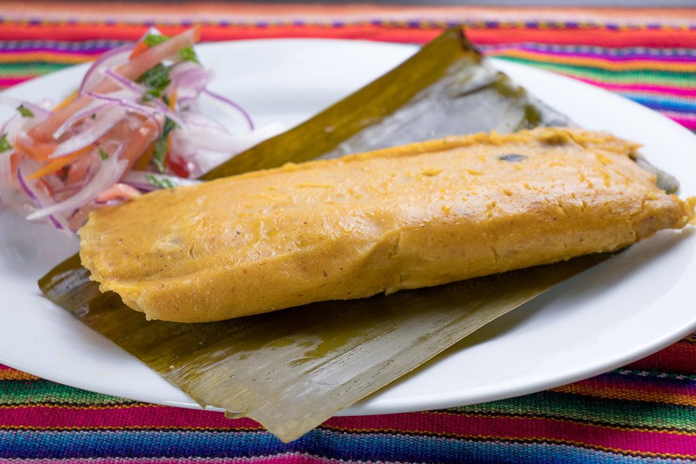 Traditional Peruvian tamales wrapped in banana leaves, filled with seasoned pork and corn dough, served with salsa criolla